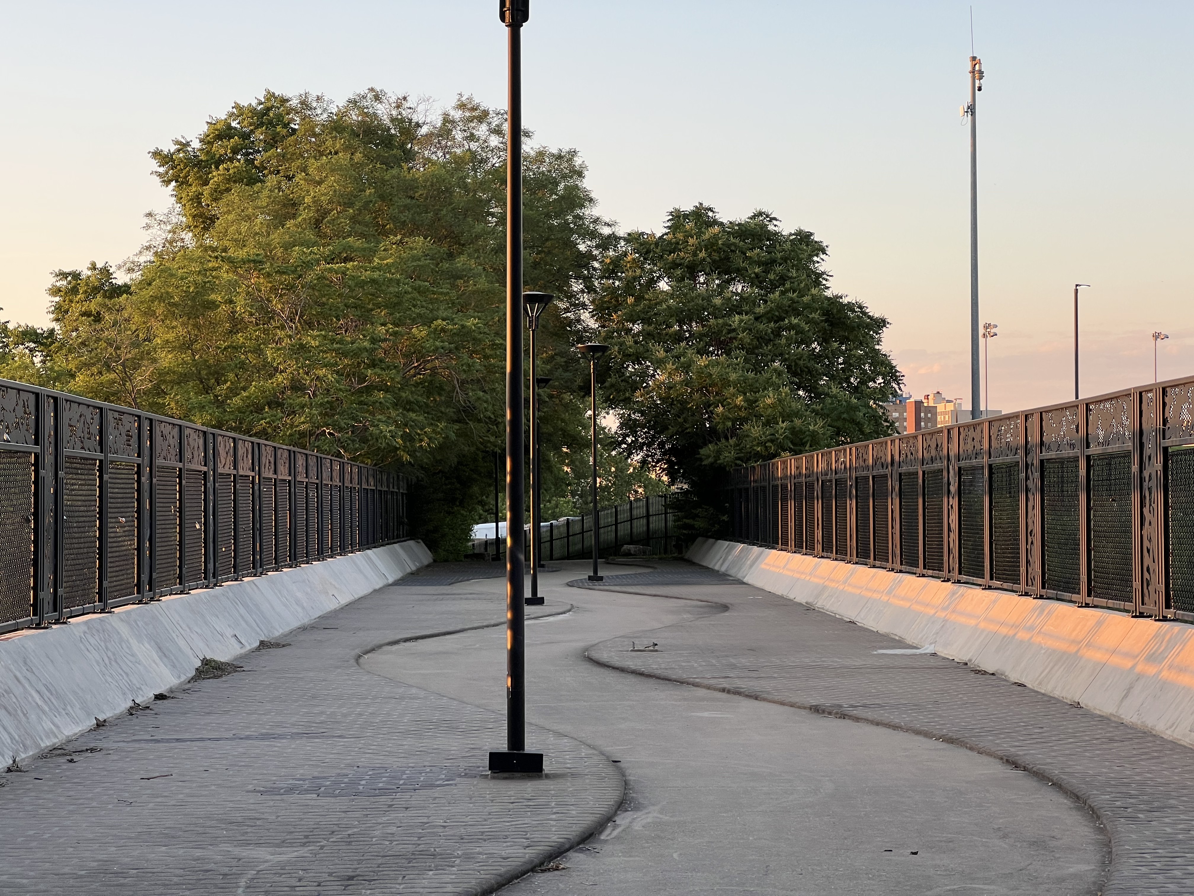Picture of a winding concrete path on a bridge with lightposts in the bends